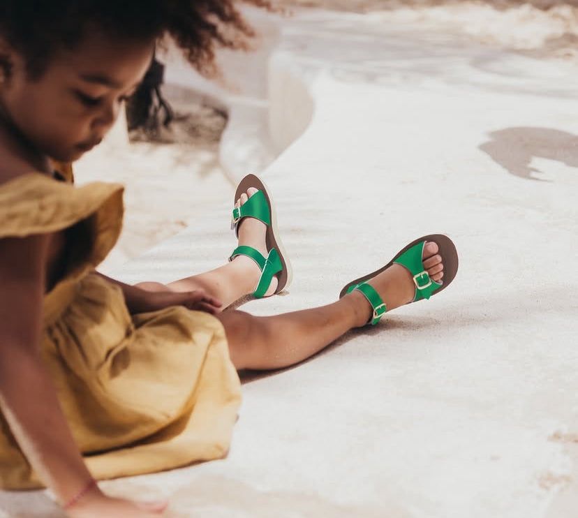 Kind in zomerkleedje met groene lederen sandalen van Anna Pops op een zonnige dag