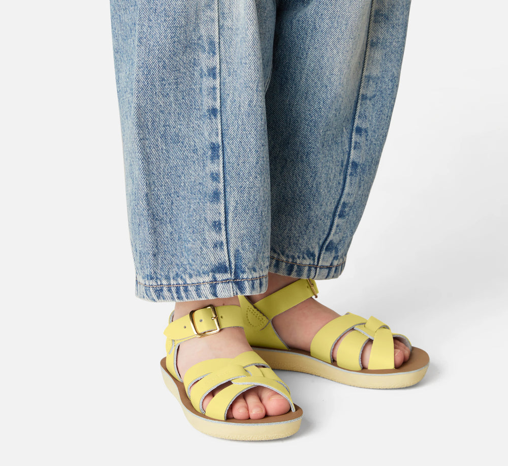 Gele Salt Water kindersandalen gedragen door kind, met jeansbroek en gespsluiting
