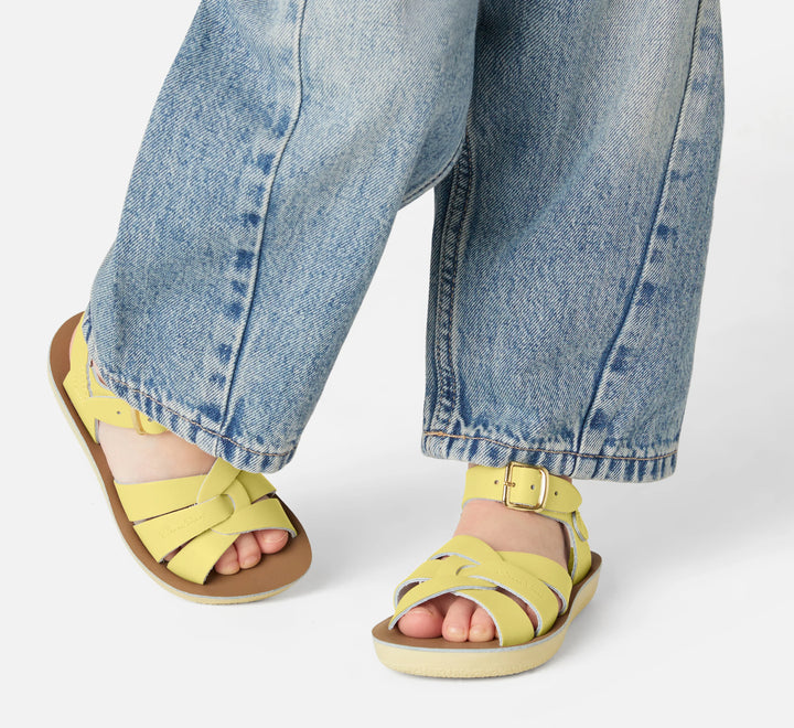 Kind met gele Salt Water sandalen in beweging, retro design met gevlochten bandjes