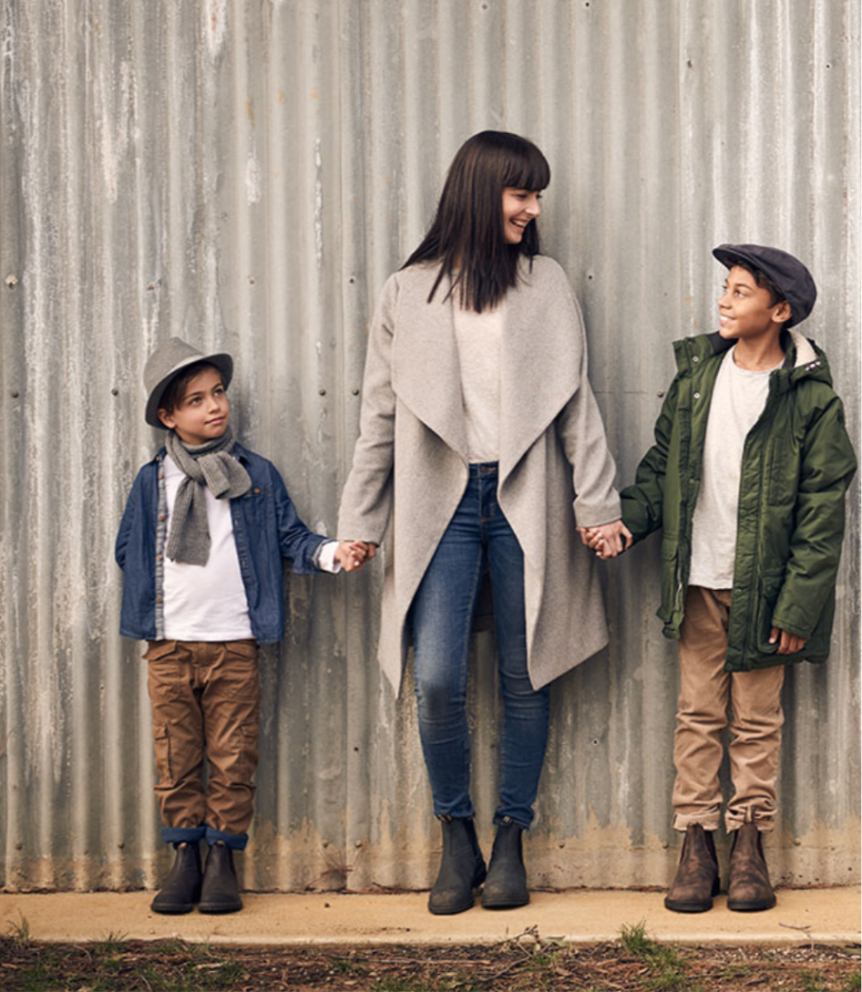 Vrouw en twee kinderen dragen Blundstone Classic Forest 2442 laarzen, staand voor metalen wand, casual outdoor kleding
