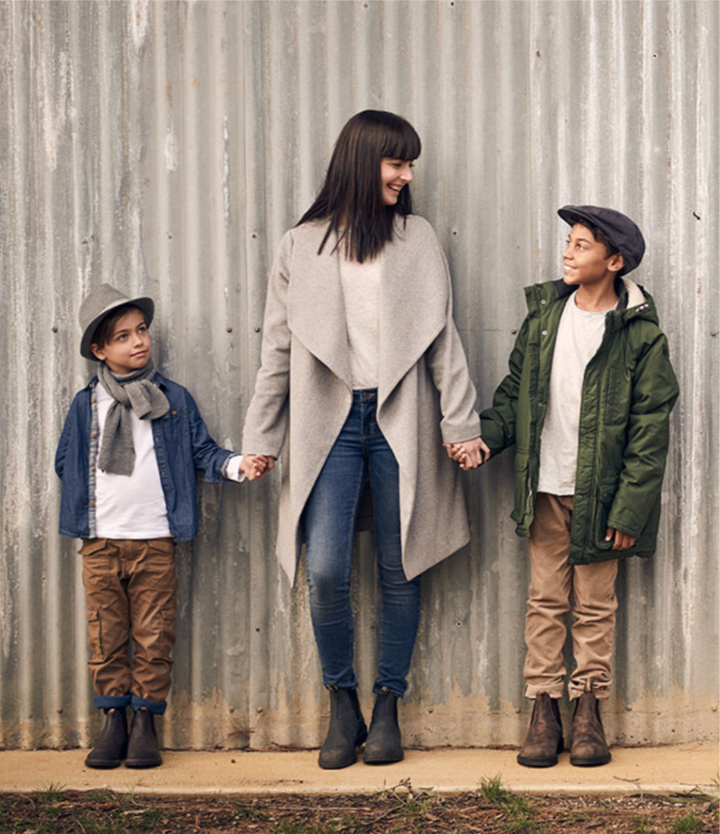 Vrouw en twee kinderen dragen Blundstone Classic Clay 2446 laarzen, staand voor metalen wand, casual outdoor kleding