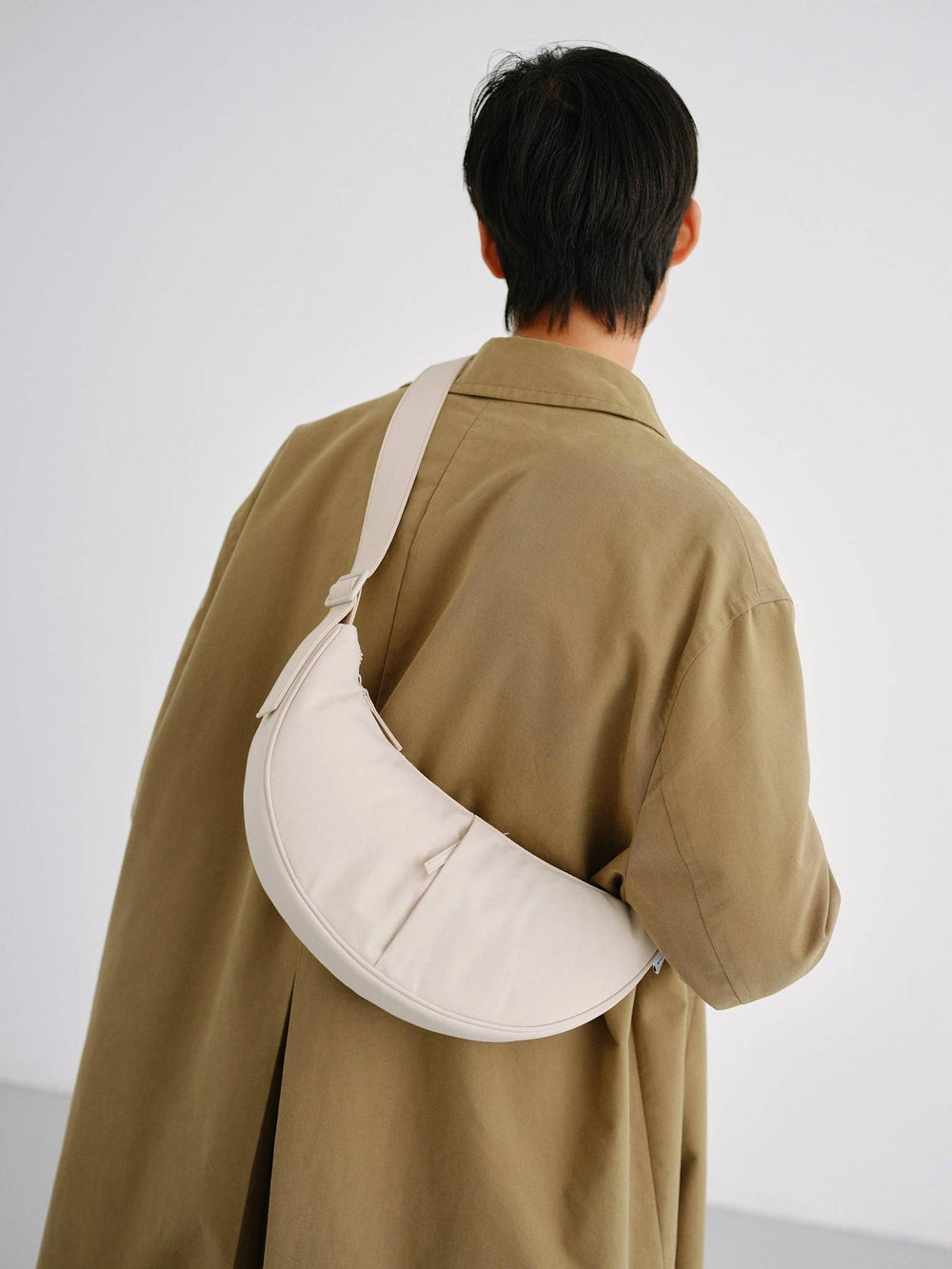 Zandkleurige Olend Moon schoudertas gedragen als crossbody over de rug door een persoon in beige jas