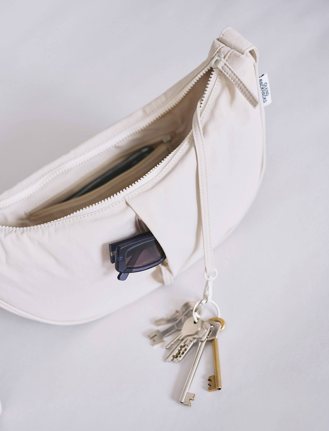 Detail van zandkleurige Olend Moon crossbodytas met sleutelhanger en zonnebril in voorvak